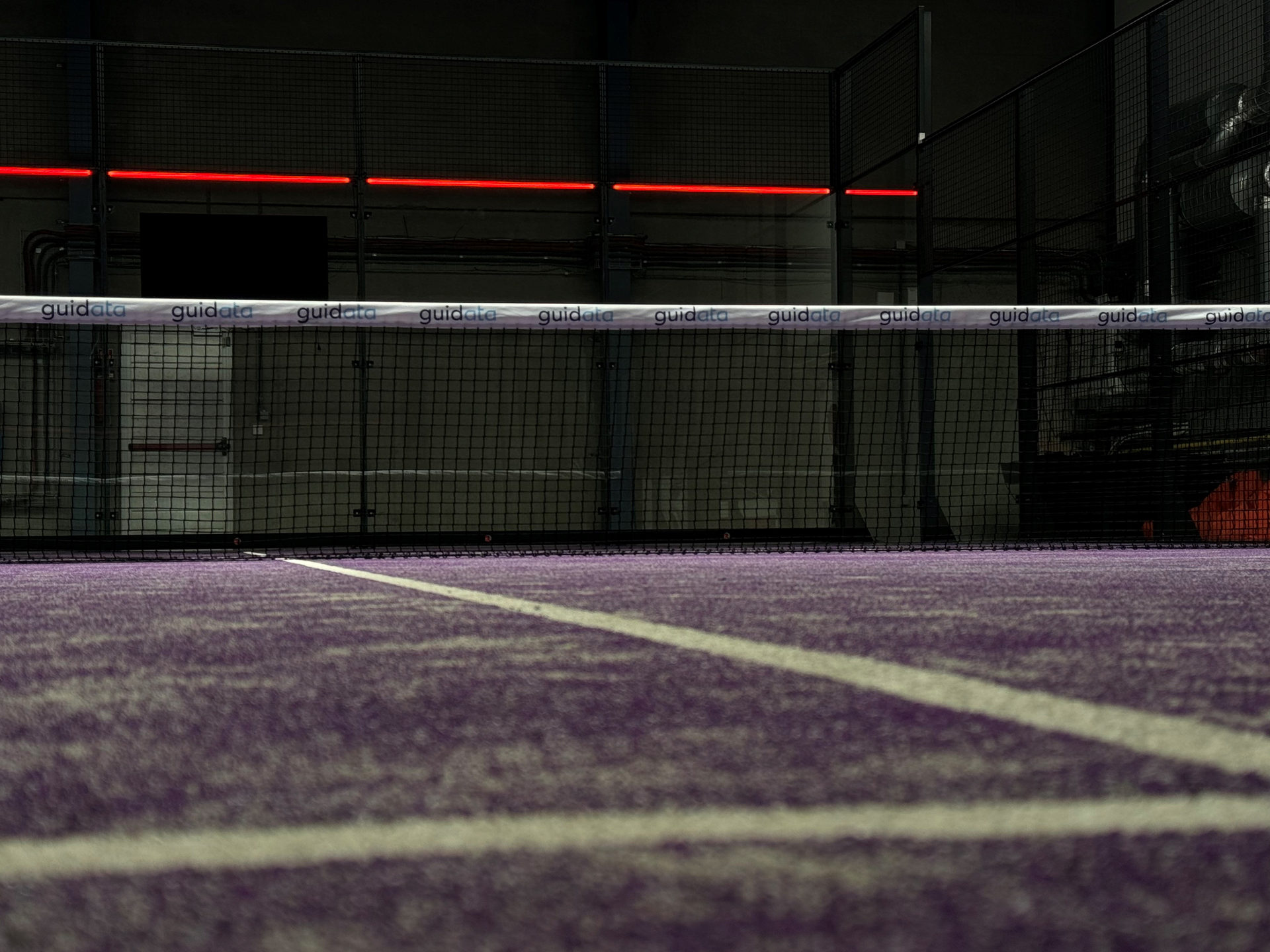 Rode Reddpoint-lijnen lichten op boven de glaswand van een padelbaan